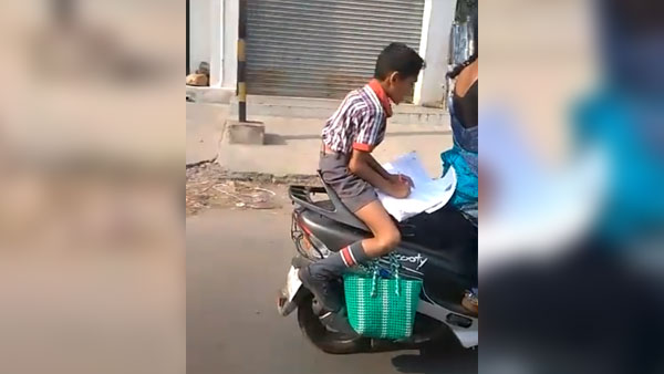 కదిలే స్కూటర్ మీద హోమ్ వర్క్ చేస్తున్న పిల్లాడు